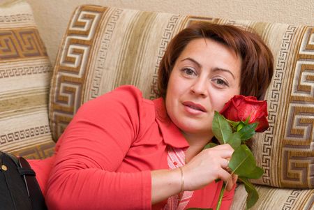 Woman with rose rests upon sofaの写真素材