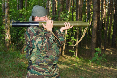 Young man in a camouflage shoots from a grenade launcher