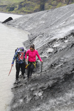 ICELAND - JULY 4, 2016: Tour guide helping tourist during glacier walk at Solheimajokull glacier. Solheimajokull glacier is one of the biggest glaciers in Europe.のeditorial素材