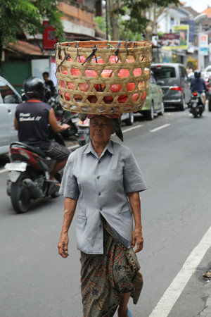 BALI, INDONESIA - FEBRUARY 6, 2016: Woman is walking and carrying a basket on her head on the street of Ubud in Bali. Indonesiaのeditorial素材