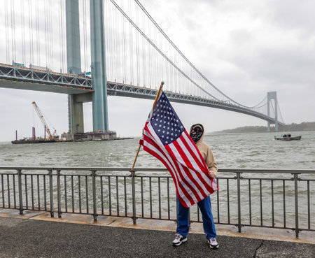NEW YORK - APRIL 30, 2020: Flag-bearing spectator salutes on the Brooklyn shoreline as the USNS Comfort Hospital Ship departing New York City after a month of caring for patients with the Coronavirusのeditorial素材