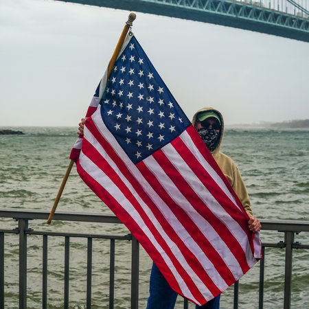 NEW YORK - APRIL 30, 2020: Flag-bearing spectator salutes on the Brooklyn shoreline as the USNS Comfort Hospital Ship departing New York City after a month of caring for patients with the Coronavirusのeditorial素材