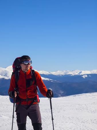 The man with trekking poles is in the mountains in winter.の写真素材
