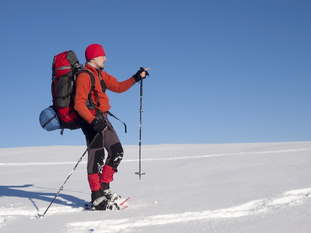 The man in snowshoes and with trekking poles indicates the direction in the mountains.の写真素材