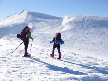 Men in snowshoes and with trekking poles go in the mountains.の写真素材