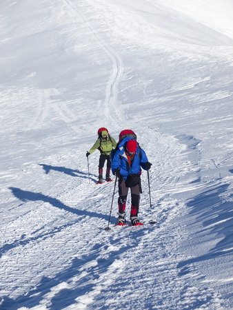Men in snowshoes and with trekking poles go in the mountains.の写真素材