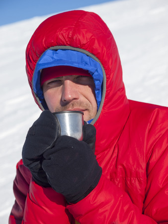 Man drinking from a mug in the mountains in winter.の写真素材