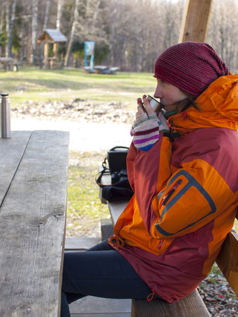 Girl sitting at a wooden table and drinking from a thermos.の写真素材