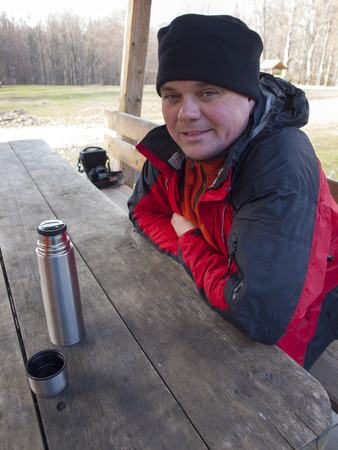 A man with a thermos sitting at a wooden table in the forest.の写真素材