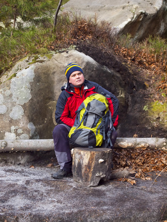 A man with a backpack resting in the forest, sitting on a log.の写真素材
