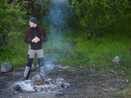 A man stands near a fire on a background of green forest.の写真素材