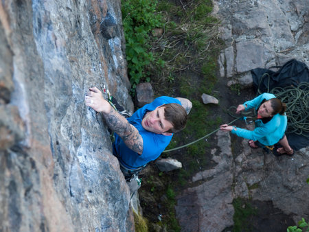 The man with the tattoos is engaged in rock climbing and climbs on the rock.