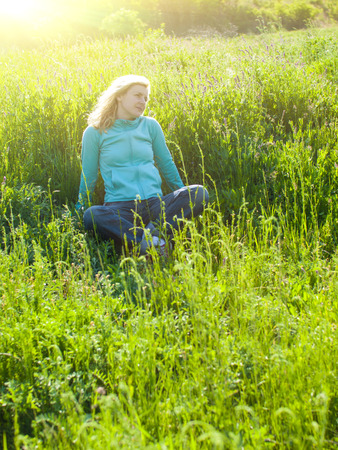 Portrait of young beautiful girl in a knitted cap in a grassy field at sunset.の写真素材
