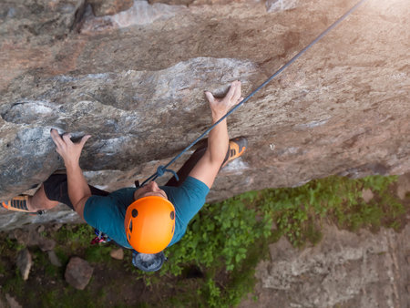 The climber in orange protective helmet difficult climbs on the wall.の写真素材