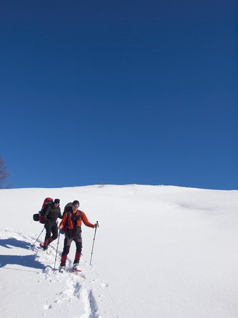 Men friends with snowshoes and big backpacks are in the mountains in the snow.の写真素材