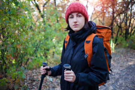 Young woman walking in autumn forest with a backpack.