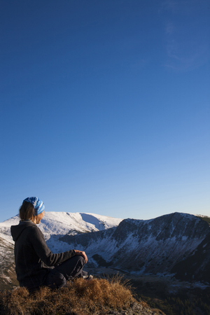The girl sits on stone and looks at mountains.の写真素材