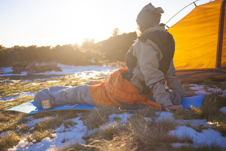 Girl sitting in a sleeping bag with a phone and a drink.の写真素材