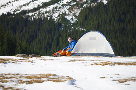 Tourist sitting near a tent and a backpack on a background of mountains.の写真素材