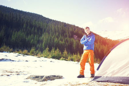 A tourist stands near a tent and a backpack on a background of mountains.の写真素材