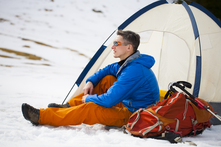 A tourist stands near a tent and a backpack on a background of mountains.の写真素材