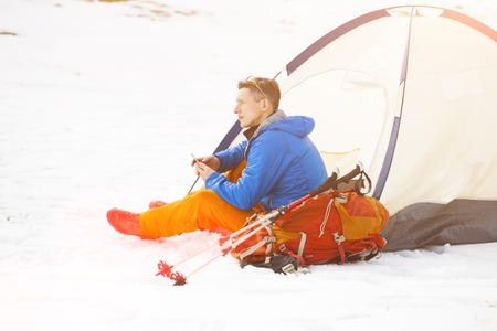 A tourist stands near a tent and a backpack on a background of mountains.の写真素材