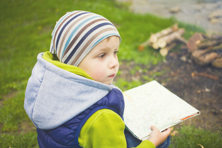 The child who is traveling is looking at a map sitting near a fire in a clearing.の写真素材