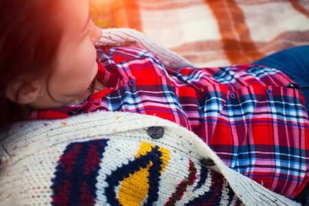 Girl in plaid shirt and sweater lying on the blanket.