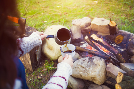 The girl prepares coffee by the fire in nature in the camping.の写真素材