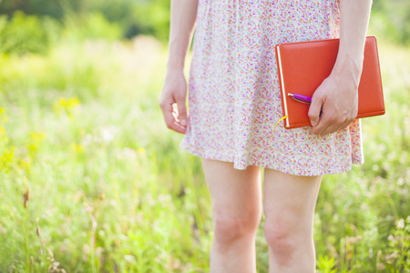 Girl in summer dress holding a book standing on the Sunny meadow. Soft focus.の写真素材