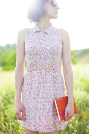 Girl in summer dress holding a book standing on the Sunny meadow. Soft focus.の写真素材
