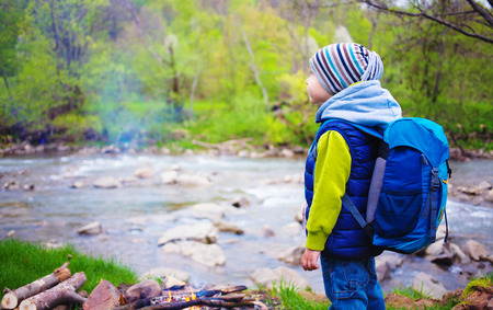 A little boy with a backpack standing on the banks of the river.の写真素材