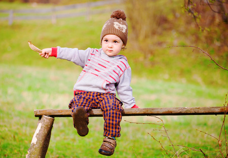 A little boy is sitting on a Park bench under a tree.の写真素材