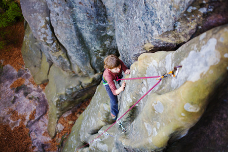 Bold kid rock climber climbs on a difficult wall.の写真素材
