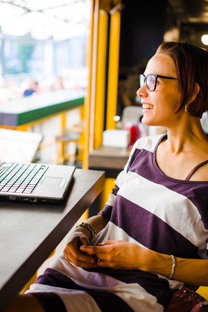 Smiling girl sitting at a table in a cafe with a laptop.の写真素材