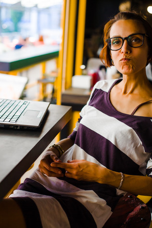 Smiling girl sitting at a table in a cafe with a laptop.の写真素材