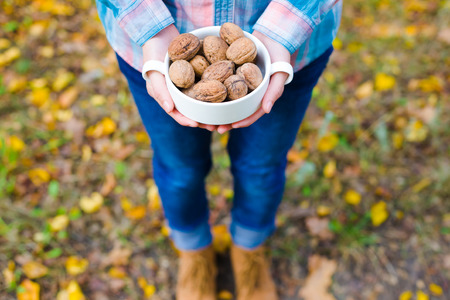 Girl holding a bowl of walnuts standing in the autumn forest. Soft focus.の写真素材