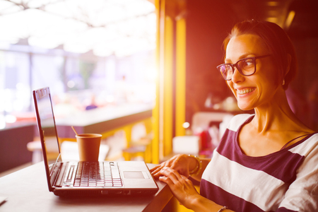 Smiling girl sitting at a table in a cafe with a laptop.の写真素材
