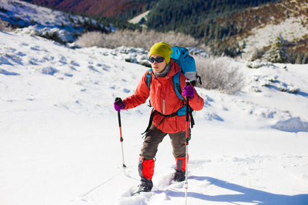 girl with backpack walking on snow in the mountains and mountain climbing during the winter holidays.の写真素材