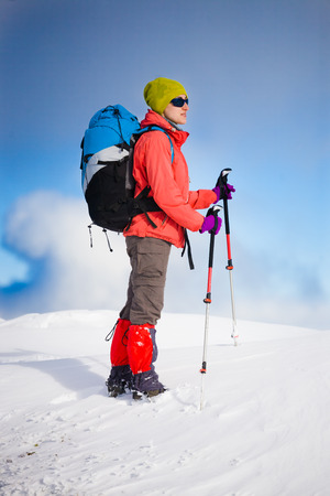 girl with backpack walking on snow in the mountains and mountain climbing during the winter holidays.の写真素材