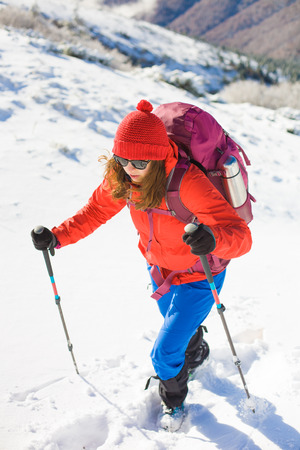 girl with backpack walking on snow in the mountains and mountain climbing during the winter holidays.の写真素材