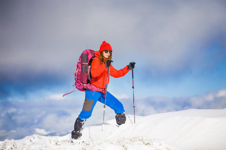 girl with backpack walking on snow in the mountains and mountain climbing during the winter holidays.の写真素材