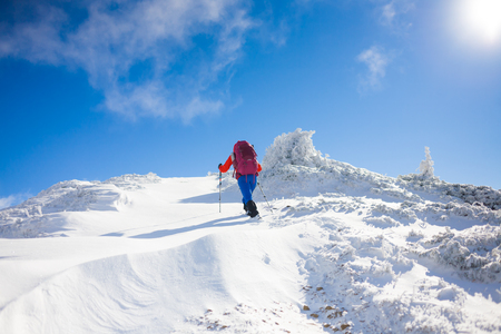 girl with backpack walking on snow in the mountains and mountain climbing during the winter holidays.の写真素材