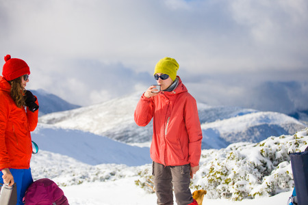 Portrait of a young girl with a Cup from the thermos in hand on background of winter mountains and blue sky.の写真素材