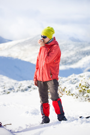 hiker with a thermos in his hands is resting during the winter ascent of the mountain.の写真素材