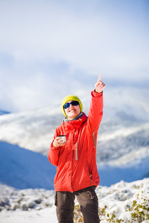 hiker with a thermos in his hands is resting during the winter ascent of the mountain.の写真素材