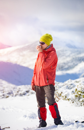 hiker with a thermos in his hands is resting during the winter ascent of the mountain.の写真素材