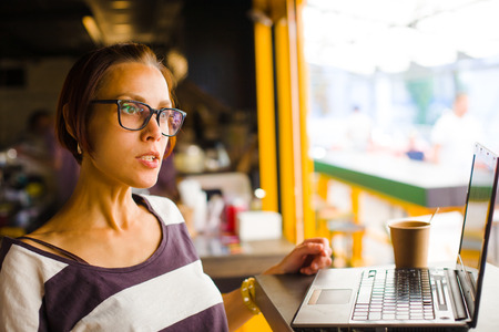 Smiling girl sitting at a table in a cafe with a laptop.の写真素材