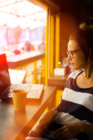 Smiling girl sitting at a table in a cafe with a laptop.の写真素材