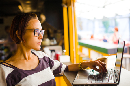 Smiling girl sitting at a table in a cafe with a laptop.の写真素材